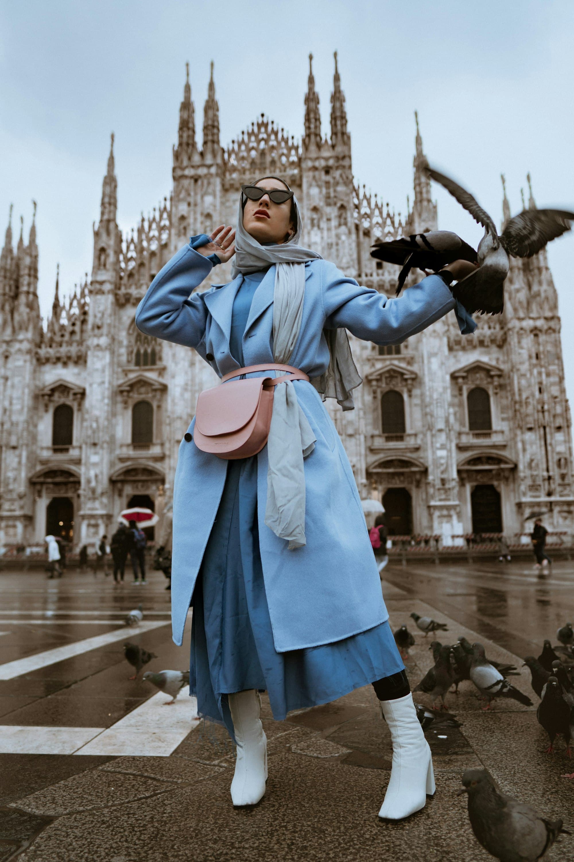 Fashion editorial — a woman in a blue coat with a designer bag before a cathedral