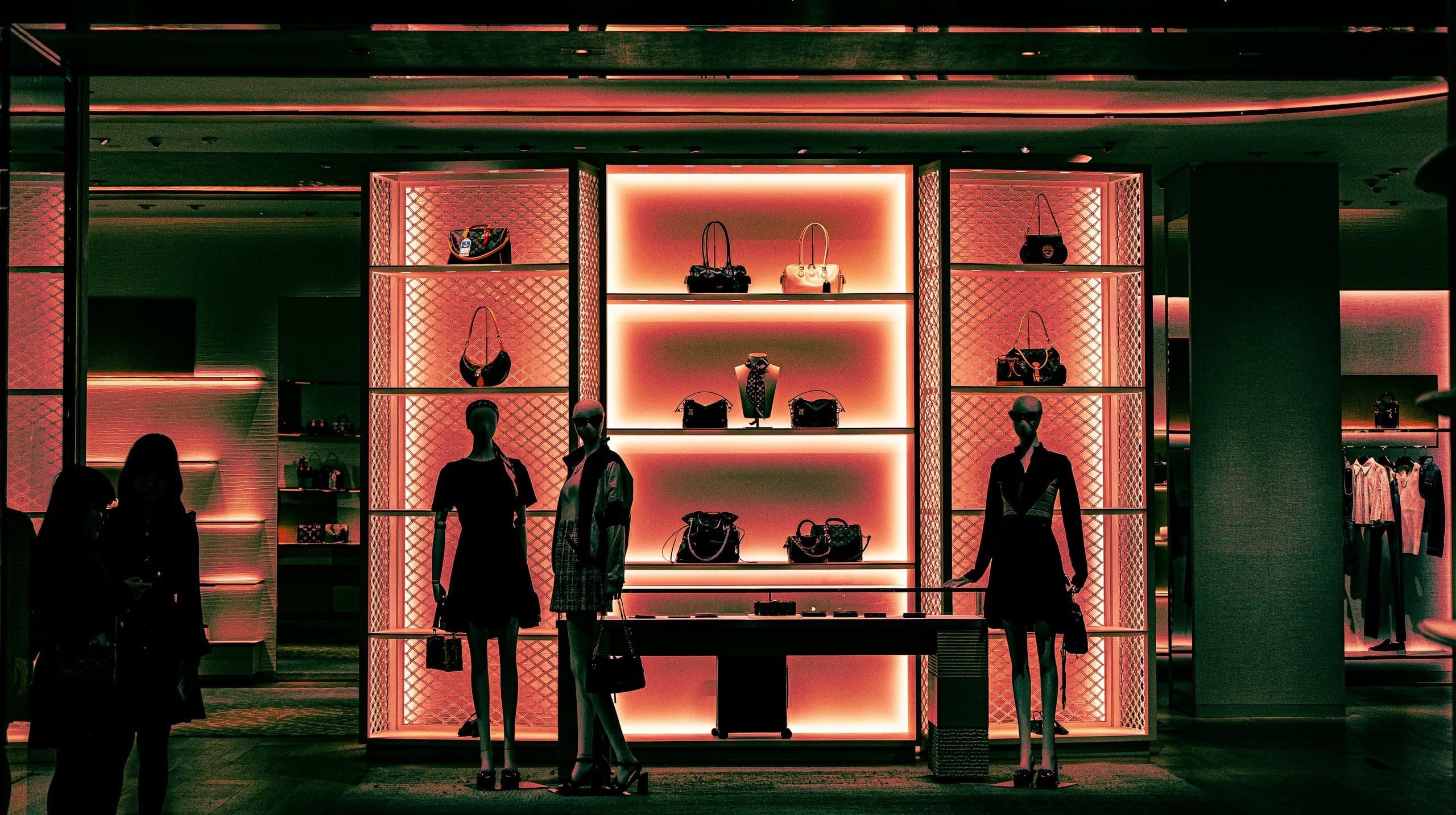 A luxury boutique aglow at night, shelves of monogram handbags flanked by mannequins