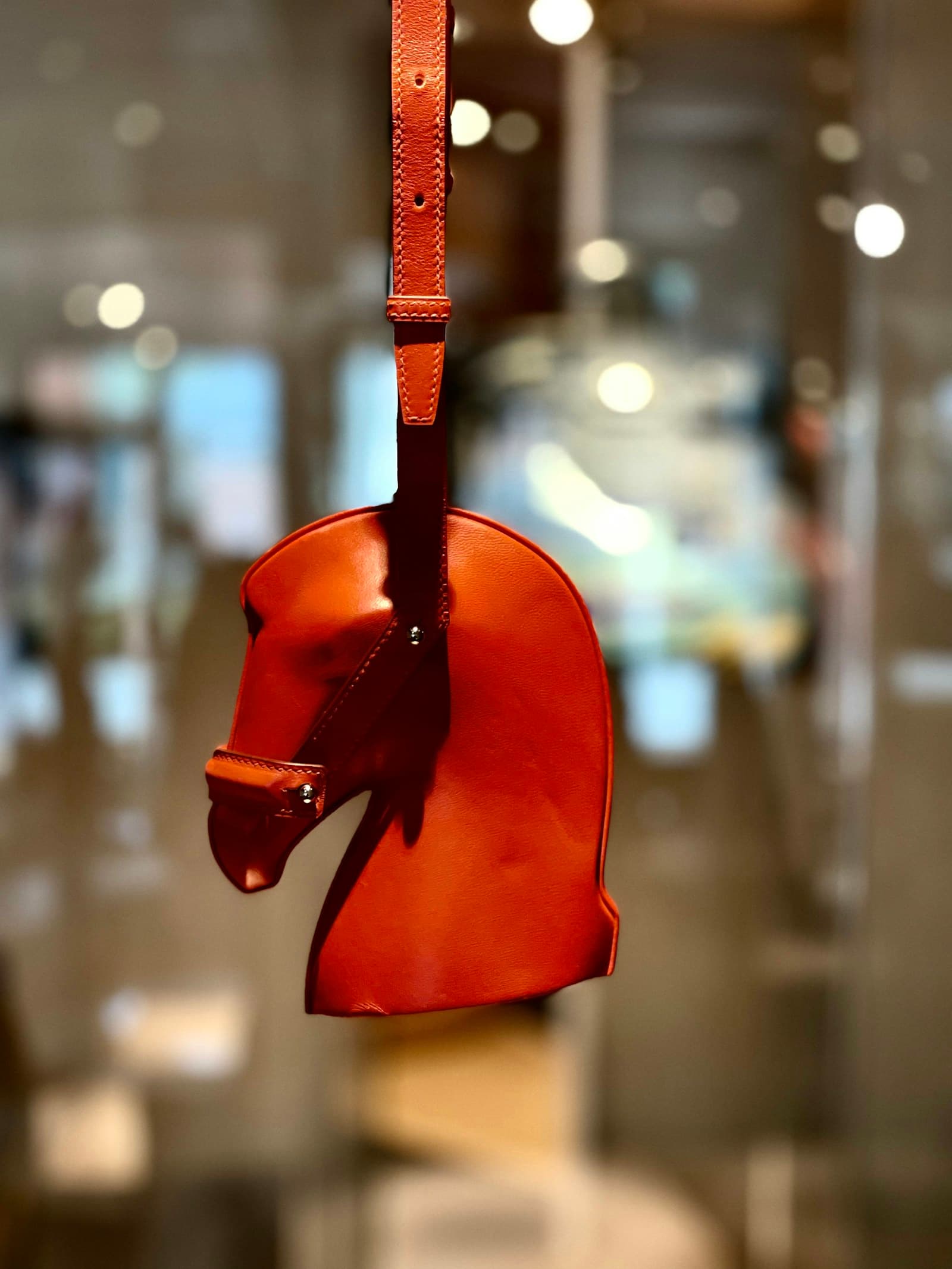 An orange Hermès leather horse charm in a glass boutique display