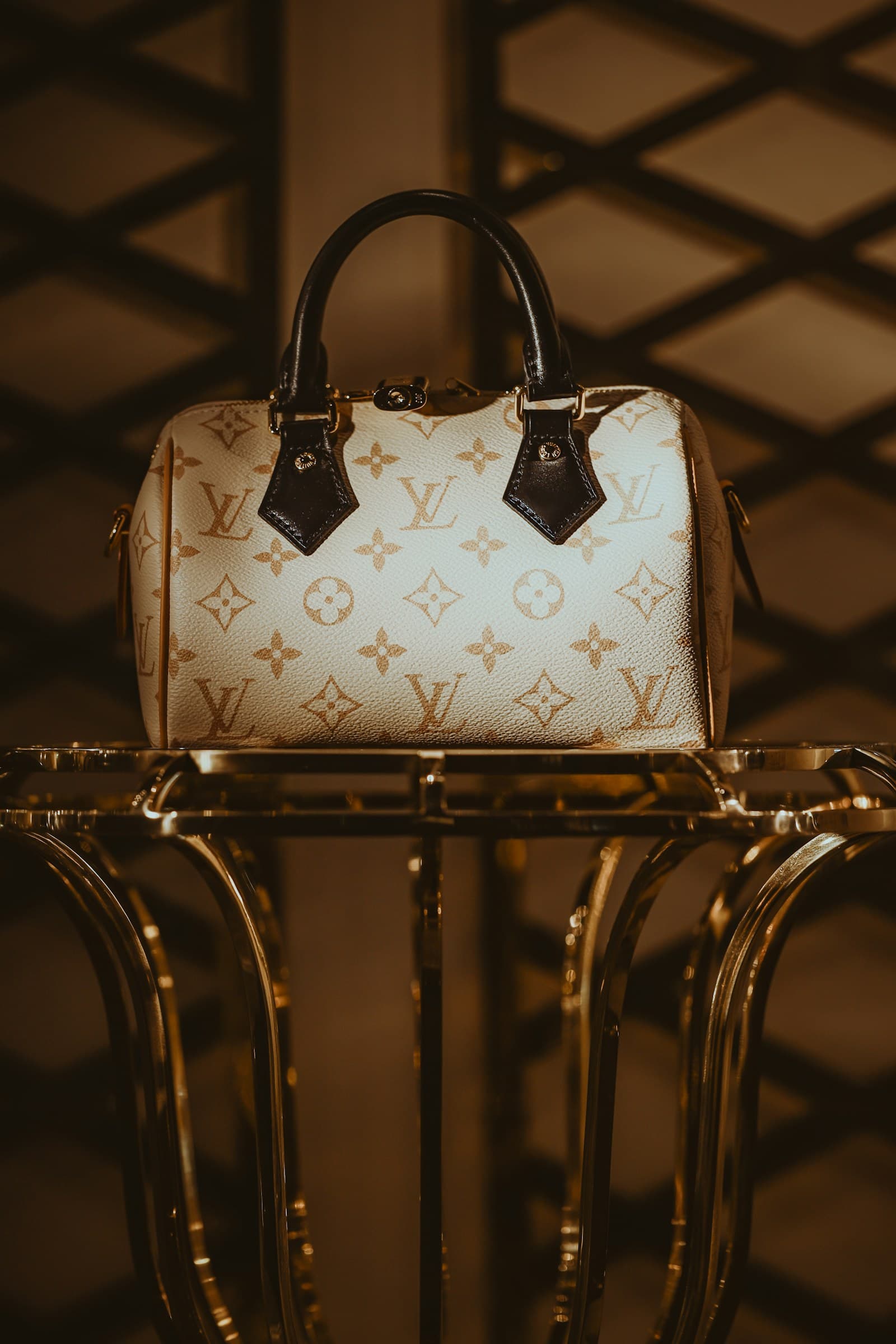 A white Louis Vuitton monogram handbag displayed on a golden stand
